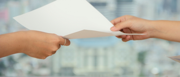 Person handing sheet of white paper to another person