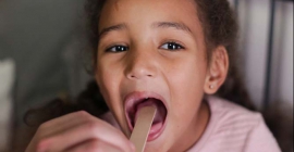 Girl with tongue depressor in open mouth